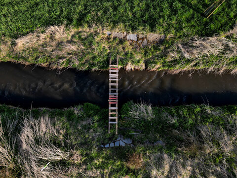 cross-country run through a flooded stream. footbridge with a thinly spaced plank floor. Big water in a narrow channel, video flight over the landscape. seed congestion
