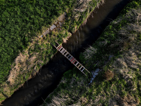 cross-country run through a flooded stream. footbridge with a thinly spaced plank floor. Big water in a narrow channel, video flight over the landscape. seed congestion