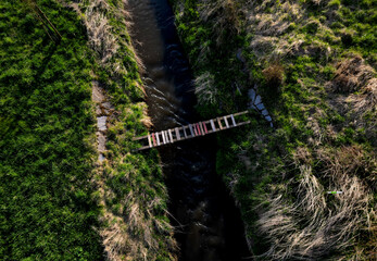 cross-country run through a flooded stream. footbridge with a thinly spaced plank floor. Big water in a narrow channel, video flight over the landscape. seed congestion