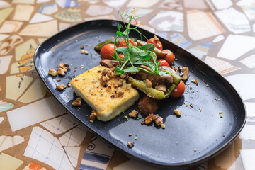 Tasty fried cheese with stewed vegetables decorating with greens on stylish plate ready for eating