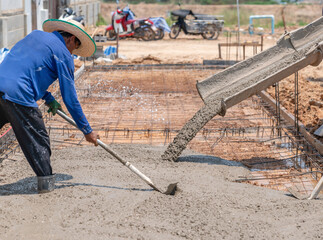 Worker spreading concrete with rakes.