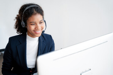 Serious call center operator in wireless headset talking to customer, woman in headphones with microphone consulting customer on phone in customer support service, looking at computer screen.