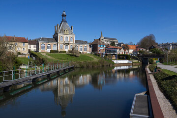 Fototapeta na wymiar View of the River Somme and Long Town Hall in the village of Long, in the Somme department, near Abbeville in France. Sunny spring day with clear sky and reflections in the still water.