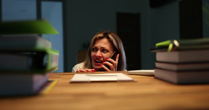 Scared woman calls police by phone explaining dangerous situation. Terrified employee feels afraid to stay alone in dark office in late evening