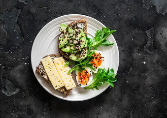 Sandwiches with avocado, cheese, seeds and boiled egg - delicious breakfast, snack on a dark background, top view