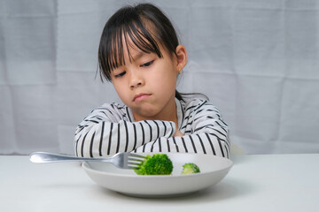 Children don't like to eat vegetables. Cute Asian girl refusing to eat healthy vegetables....