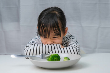 Children don't like to eat vegetables. Cute Asian girl refusing to eat healthy vegetables. Nutrition and healthy eating habits for children.