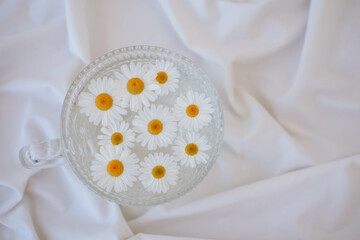 Fototapeta na wymiar Chamomile flowers in a glass bowl on white fabric background