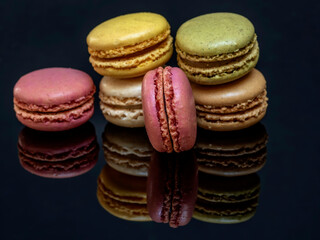 A group of delicious and colorful macarons are reflected on the glossy black support base