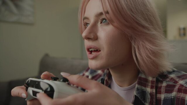 Exited Woman Playing Video Game Holding Joystick. 20s female winning video game sitting on couch at home. Happy with game victory.