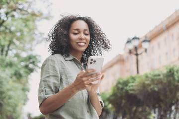 Young beautiful woman using smartphone in a city. Smiling student girl texting on mobile phone outdoor. Modern lifestyle, connection, casual business concept