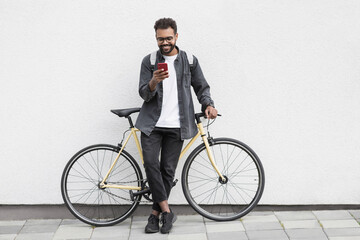 Young handsome man with bicycle over white wall background in a city, cheerful student men with mobile phone smiling outdoor, Modern lifestyle, travel, casual business, connection concept