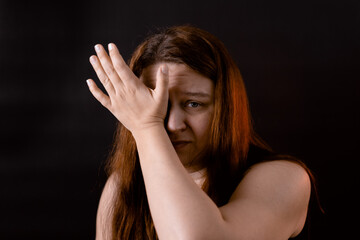 Obraz premium Crying sad young woman wiping eyes with hand. Female portrait isolated on black. Upset girl suffering from pain. Feelings, life difficulties. Human emotions, facial expression concept.
