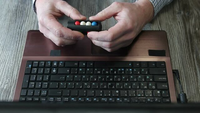 A man sits at a laptop and holds a puzzle game in his hands.