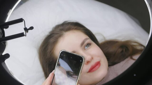 Photo video shooting on a cell phone beautiful girl model after permanent lip makeup. Young woman with beautiful lips after tattooing posing for smartphone camera after procedure