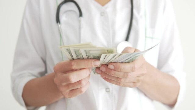 Close-up, a female doctor in a white coat counting a pack of 100 dollar bills