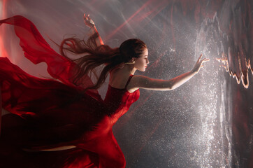Fantasy mystery woman swims underwater touches magic light mirror, looks into reflection. Fairy tale Beauty Girl princess sleeping soars floating in dream dark water. Art ballerina dancing red dress - obrazy, fototapety, plakaty
