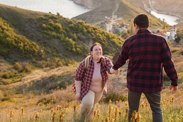 Tourists: A couple travels through the spring mountains. A man in a plaid shirt gives his hand to help a plump woman up the mountain. Walks in the open air. Travel and active life concept. Travel life