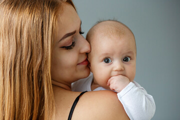 Mother takes care of newborn baby at home. Smiling mother holds two month old daughter in arms. Kiss