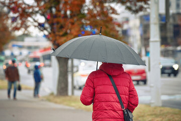Man with black umbrella walk on city street in rainy day. Alone man with umbrella. Back view of stylish man in rainy weather walkin down the city street. Selective focus.
