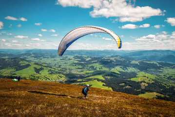 Paraglider is starting for fly. Parachute is filling with air in the mountains in sunny day.
