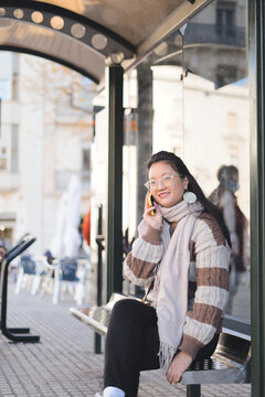 Modern and connected: A young Chinese woman enjoys a free afternoon at a bus stop while talking on the phone.