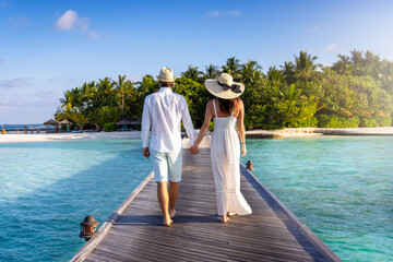 A elegant couple walks down a wooden pier over turquoise sea in the Maldives islands during their romantic holiday time - obrazy, fototapety, plakaty