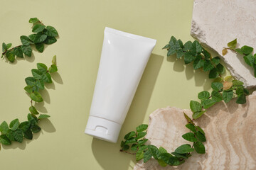 A white tube displayed with some stones and green leaves. Mockup of skin care cosmetic tube of...