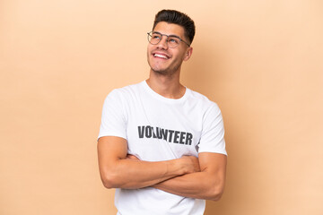 Young volunteer caucasian man isolated on beige background looking up while smiling