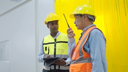 Two professional factory warehouse workers holding tablet and radio communication talking and...