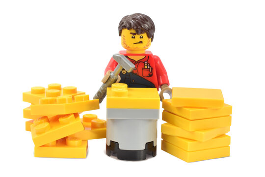 Lego minifigure of worker in uniform holds a hammer in a hand and makes flat bricks. Editorial illustrative image of remake job or stupid work occupation.