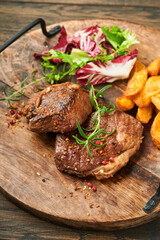 Steaks. Sliced grilled meat steak New York, Ribeye or Chuck roll with with garnished with salad and french fries on black marble board on old wooden background. Top view. Mock up.
