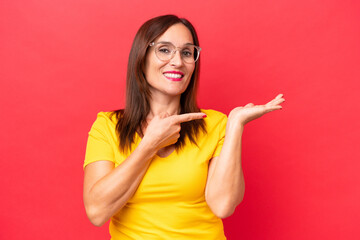 Middle-aged caucasian woman isolated on red background holding copyspace imaginary on the palm to...