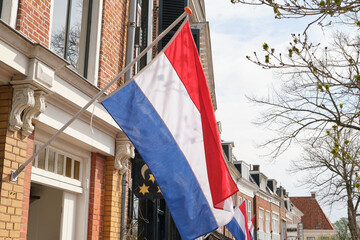 Dutch flags waving in a typical dutch street on Koningsdag under a blue sky. Koningsdag is a national holiday in the Kingdom of the Netherlands.