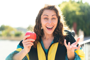 Young sport woman with an apple at outdoors with shocked facial expression