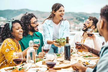 Happy friends dining and drinking red wine glasses on balcony rooftop party - Young people enjoying lunch break at restaurant terrace - Youth lifestyle moments concept with guys and girls hanging out