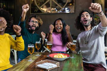 Diverse group of four young adult friends watching football on TV in sport bar