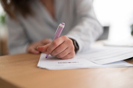 High angle of crop anonymous female in casual clothes sitting at wooden table checking printed expenses bill next to a computer