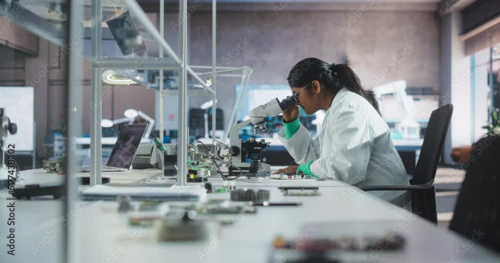 Poster Young Indian Science Student Conducting Electronics Experiment in a University Workshop. Diverse Young Scholar Using Microscope, Working on Connecting a Circuit Board