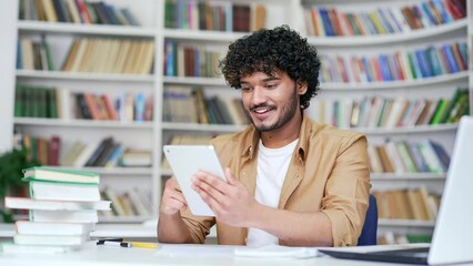 University student using tablet in campus library space. Happy college teacher looking for information on the internet or chatting with a friend, writing a text message, checking email or social media