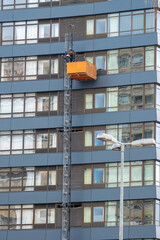 Maintenance workers on a hanging cradle or lifting platform carrying out repair work on the facade...