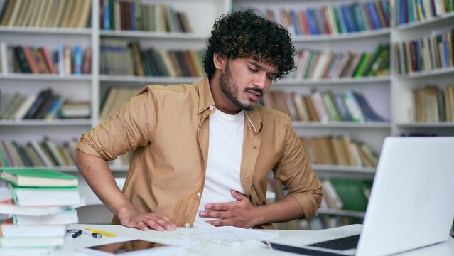 Student suffering from stomach pain while working on laptop while sitting in campus library space. The male has problems with digestion, poisoning, stomach ulcer, gastritis, constipation or spasms