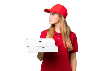 Young caucasian pizza delivery woman with work uniform picking up pizza boxes over isolated background looking to the side