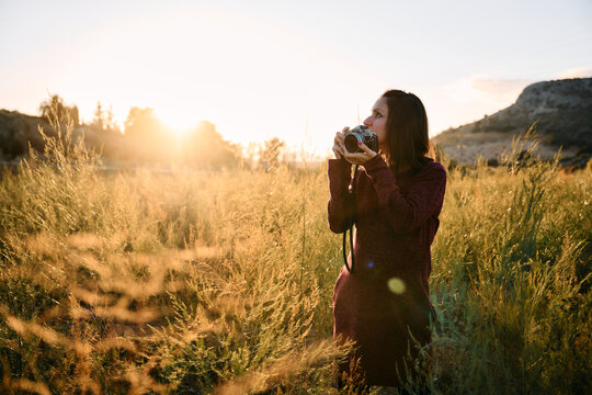 A young woman strolling through the countryside with her vintage camera at sunset.