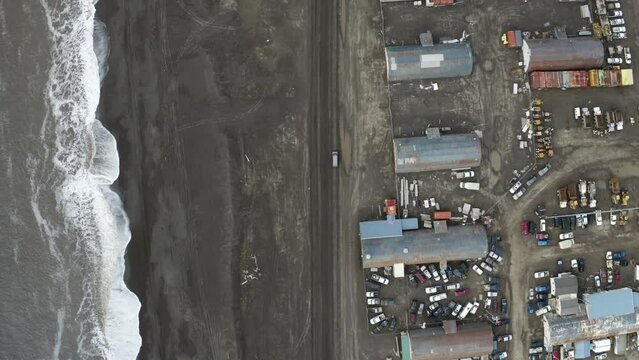 Aerial Top Down Tracking Drone shot of Van Driving along Flooding Road next to the Arctic Ocean and Run Down Structures near Barrow Alaska
