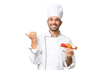 Young caucasian chef holding a sushi over isolated background pointing to the side to present a product