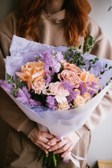 Very nice young woman holding big and beautiful flower bouquet of fresh roses, carnations, eucalyptus and other flowers in peach and purple colors, vertical image - 597444734
