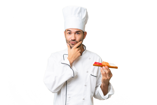 Young caucasian chef holding a sushi over isolated background thinking