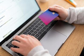 Crop anonymous female hand holding a credit card, doing online shopping on computer