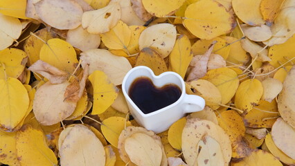 Autumn yellow leaves falling on a heart-shaped mug with coffee or tea standing on multicolored...